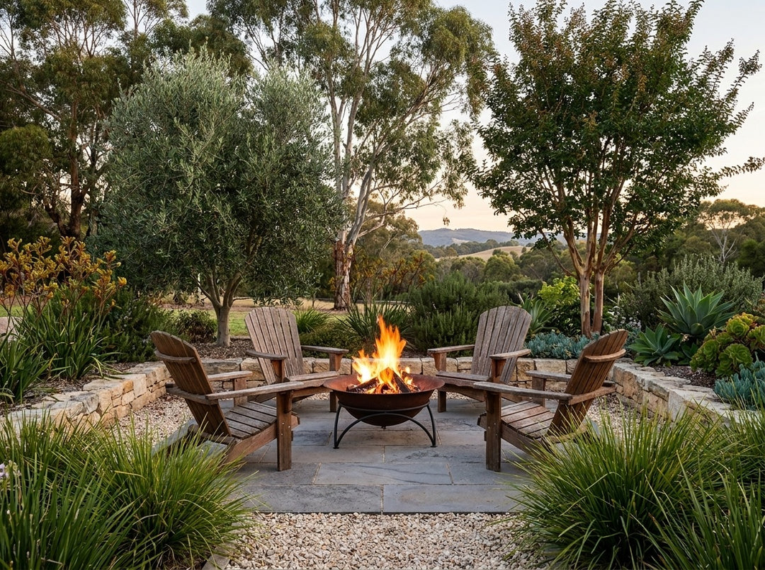Cast Iron Fire Pit, 60.5 cm across and 30 cm high, burning in a gravel fire-pit clearing in an Adelaide Hills garden at dusk with chairs drawn up around it