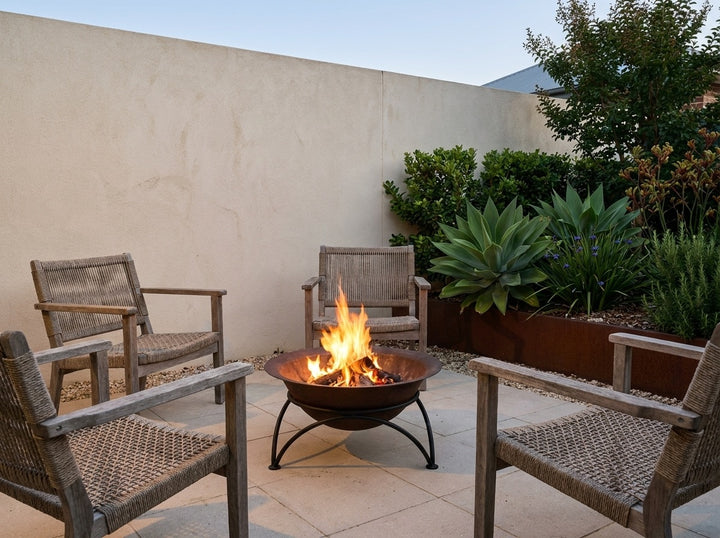 Cast Iron Fire Pit, 60.5 cm across and 30 cm high, burning in a small city courtyard at dusk with chairs drawn up around it