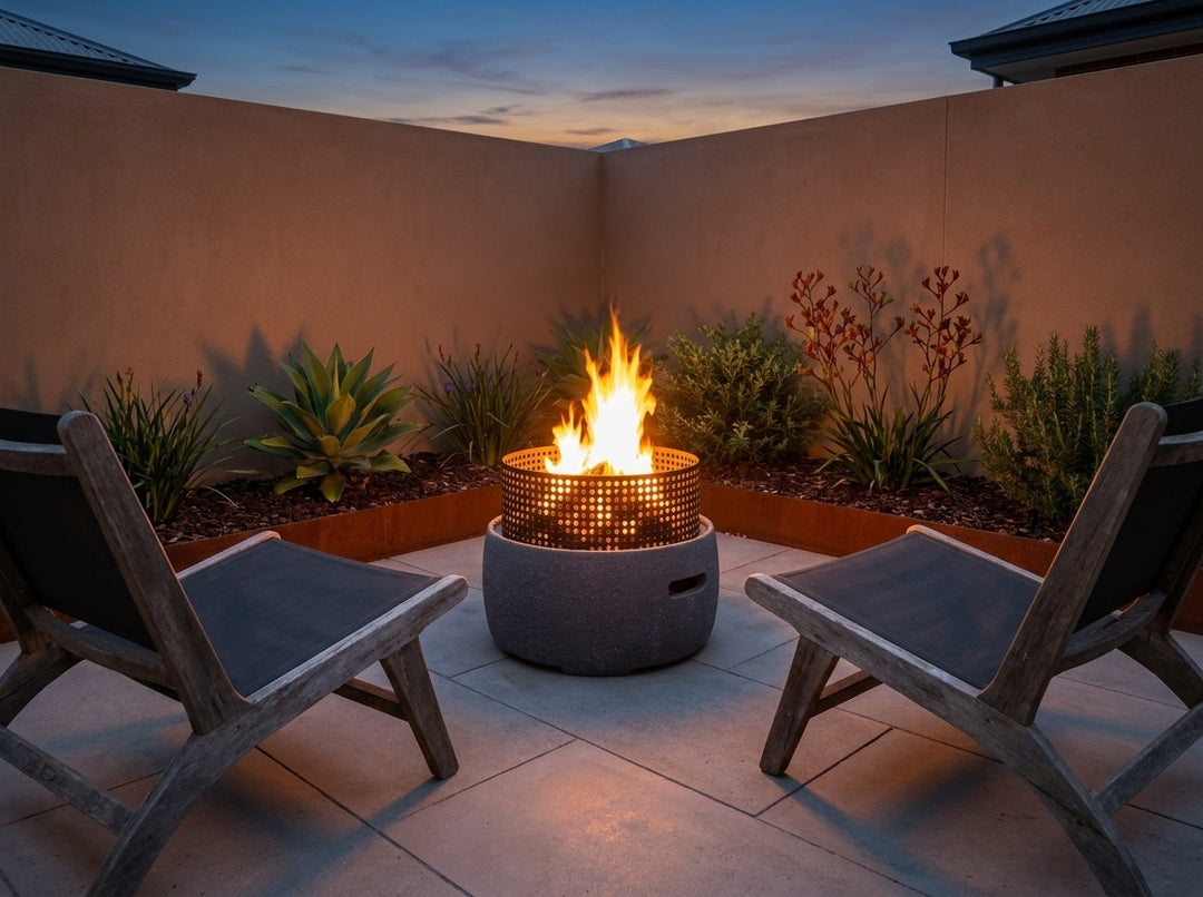 GRC Base Fire Pit, 58 cm across and 48.5 cm high, burning in a small city courtyard at dusk with chairs drawn up around it