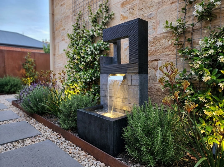 Peace Water Feature in a small city townhouse garden at dusk, water running and its integrated LED lighting glowing