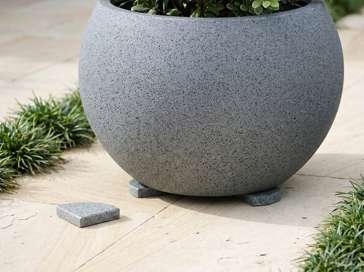 A Granite cool blue-grey terrazzo planter lifted clear of the paving on Granite pot feet, with one loose foot beside it - each foot is 70mm across and raises the pot 15mm for drainage and airflow