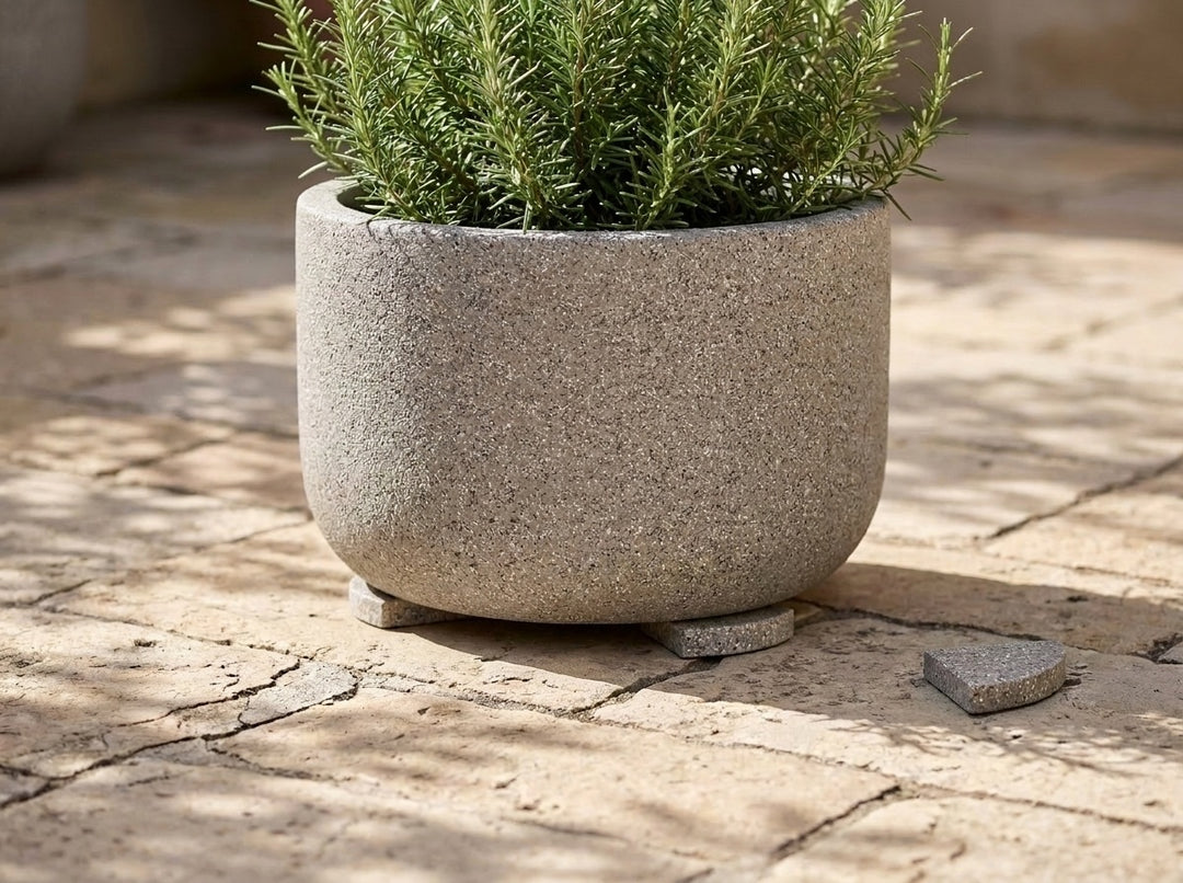 A terrazzo planter lifted clear of the paving on pot feet, with one loose foot beside it - each foot is 70mm across and raises the pot 15mm for drainage and airflow