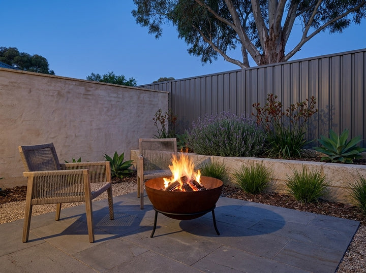 Steel Fire Pit, 61 cm across and 43.5 cm high, burning in a paved Adelaide courtyard at dusk with chairs drawn up around it