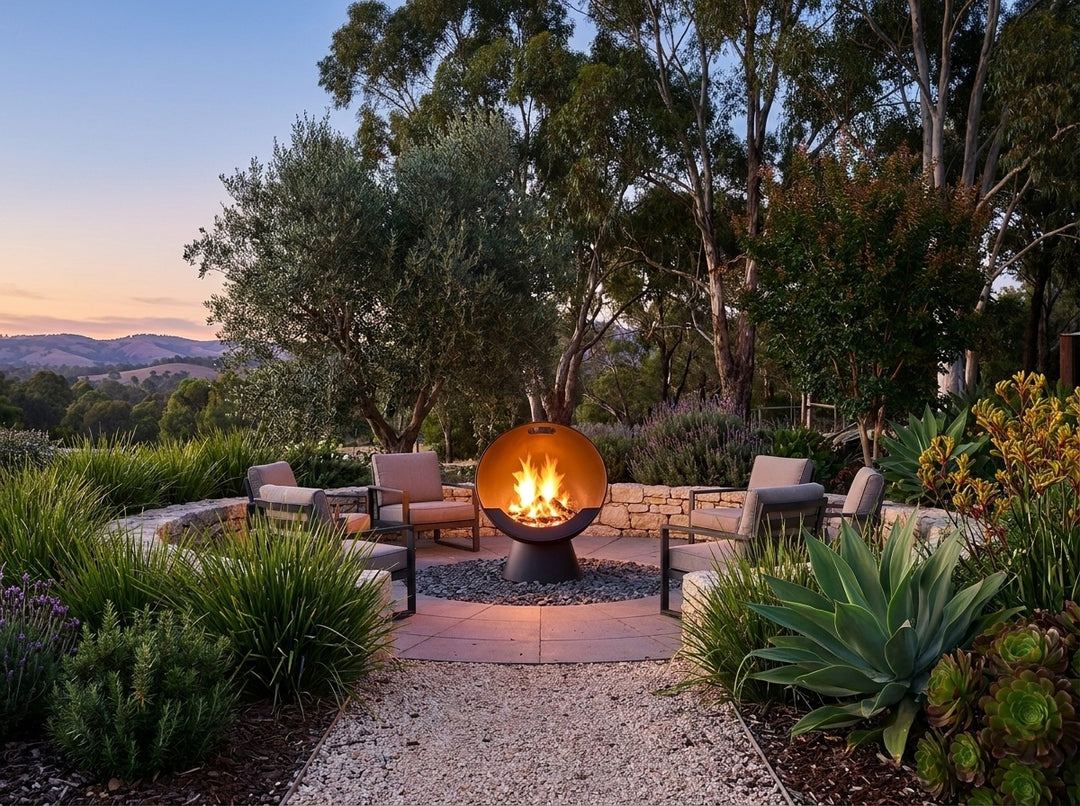 Upright Fire Pit, 61 cm across and 74.5 cm high, burning in a gravel fire-pit clearing in an Adelaide Hills garden at dusk with chairs drawn up around it
