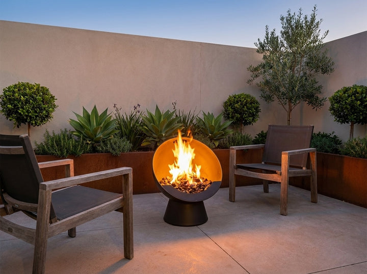 Upright Fire Pit, 61 cm across and 74.5 cm high, burning in a small city courtyard at dusk with chairs drawn up around it